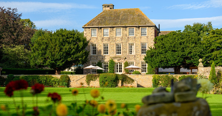 View of the grounds and gardens surrounding Headlam Hall Hotel on a bright sunny day
